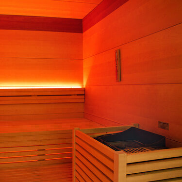 detailaufnahme mit blick in die finische sauna, die bänke die steine für den aufguß sowie warmes angenehmes licht