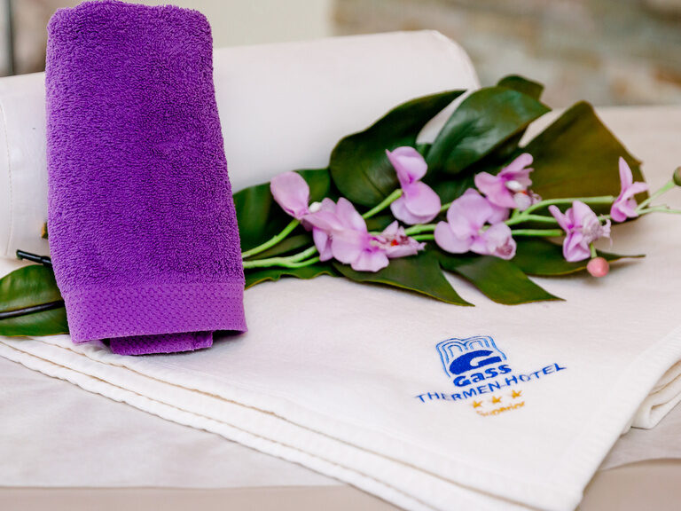 auf dem handtuch mit gass logo liegen orchideen im ein kleines lila handtuch