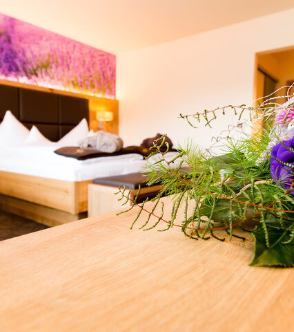 deluxe zimmer mit lila lavendel blumen als tapete über dem bett in fraben mit leihbademantel und blumenstrauß im vordergrund