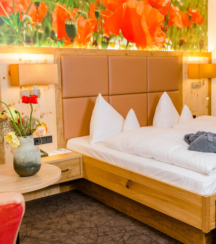 Doppelzimmer Deluxe mit Mohnblumen Wandtapete hellem holz braunen leder und bademantel auf dem bett