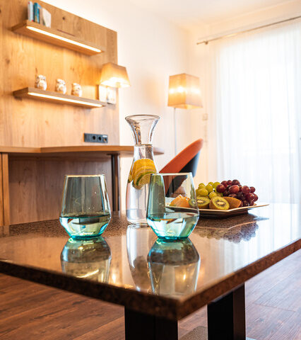 blick durch den raum auf die tvwand mit hellem holz couchtisch mit obstteller recht im bild die essecke mit orangen stühlen