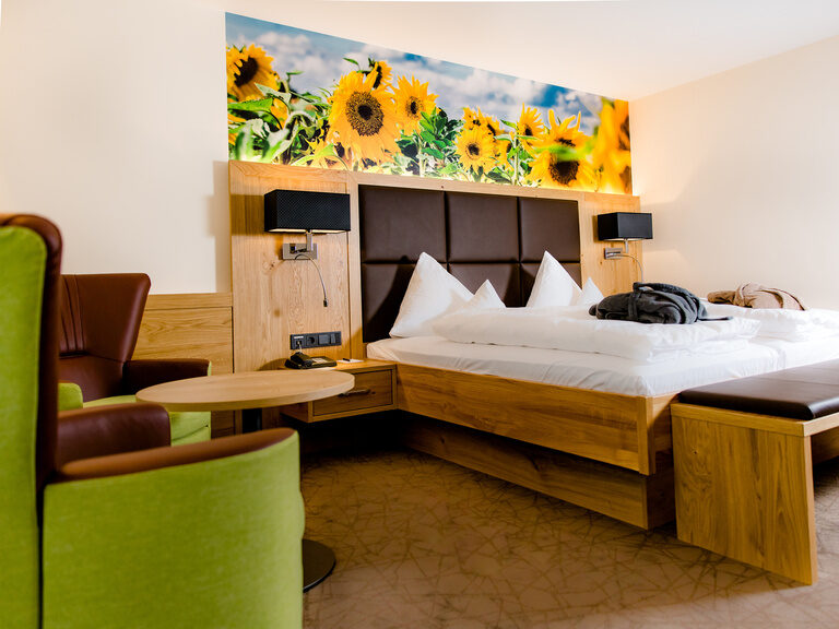 deluxe zimmer mit sonnenblumen als tapete über dem bett in warmen braun und grün mit leihbademantel