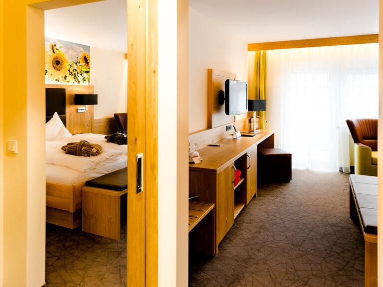 deluxe zimmer mit sonnenblumen als tapete über dem bett großer spiegel am kleiderschrank in grün und braunen farben