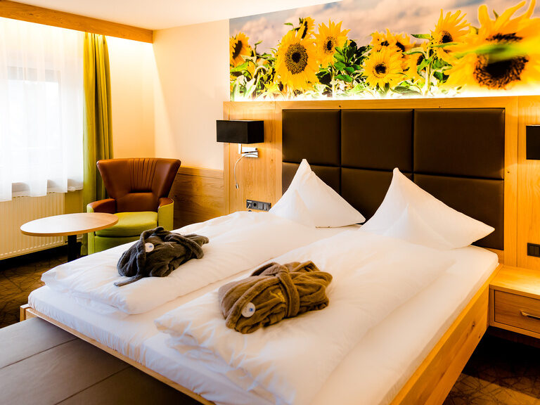 deluxe zimmer mit sonnenblumen als tapete über dem bett in grün und braunen farben mir sitzbank vorm bett helle lampen am bett