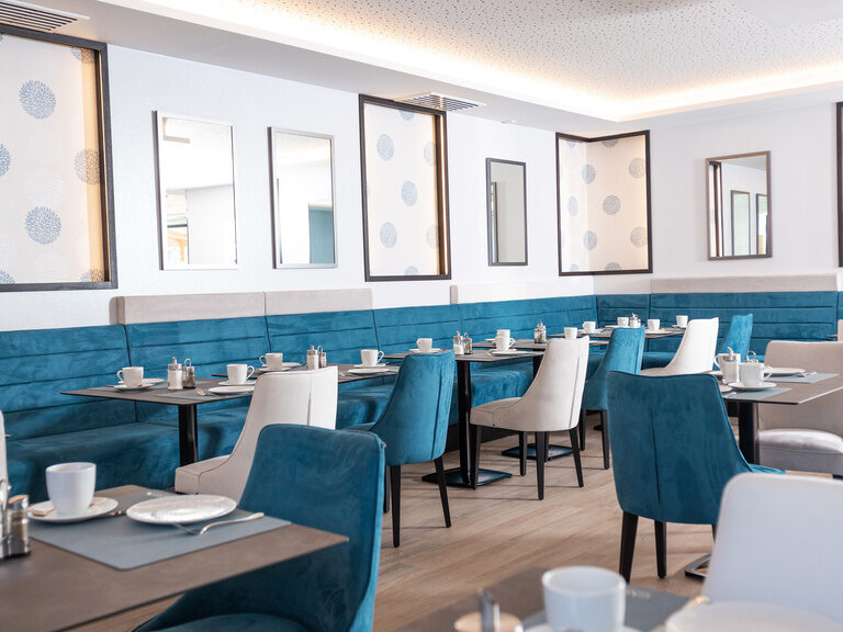 gemütliche-petrolfarbene-sitzbaenke-gedeckte-tische-spiegeln-und-beleuchtete-dekoelemente-an-der-wand