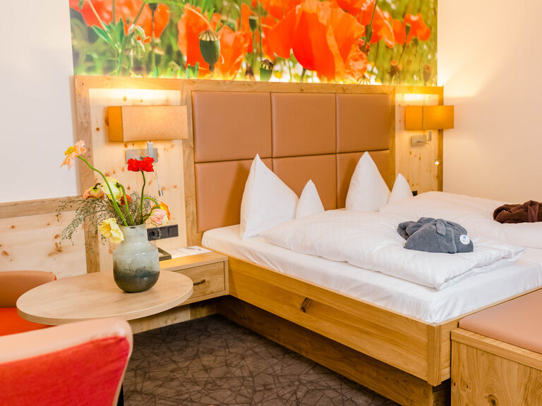 Doppelzimmer Deluxe mit Mohnblumen Wandtapete hellem holz braunen leder und bademantel auf dem bett