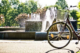 Fahrrad und Brunnen im vordergrund ein fahrrad dahinter im sonnenschein ein springbrunnen