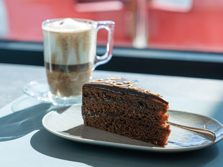 sonnenlicht-faellt-auf-die-tische-gedeckt-mit-latte-macchiato-und-saftiger-sachertorte