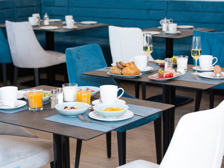 frühstücksraum mit gedeckten tischen im vordergrund früshtück mit orangensaft und dahinter sekt und herzhafte speisen