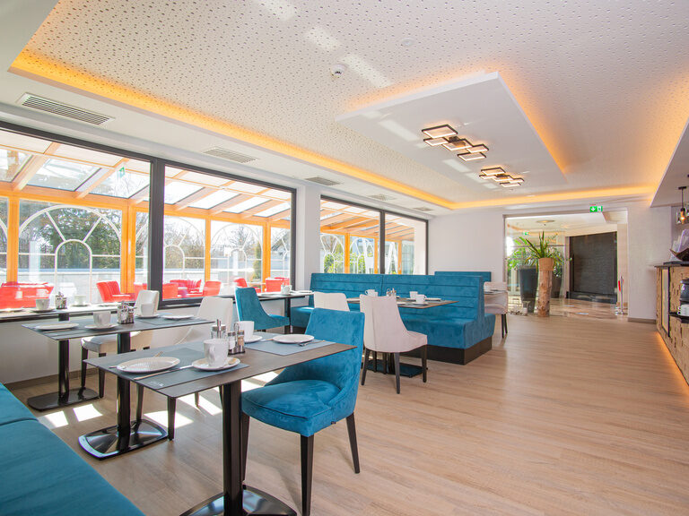 frühstücksraum mit teller und tassen gedeckt blick durch den mit roten stühlen bestückt den wintergarten zum aussenbecken