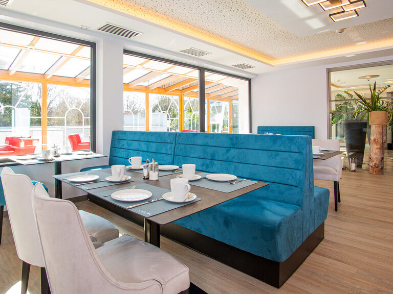 aufnahme-vom-fruehstuecksraum-mit-blick-durch-die-fenster-und-den-hellen-wintergarten-zum-aussenpool-oder-zur-lobby-mit-dem-beruhigenden-brunnen