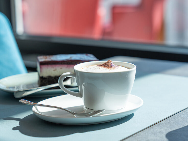 cappucino-mit-lockerem-milchschaum-einem-leckeren-hausgemachtem-kuchen-im-hellen-fruehstuecksraum