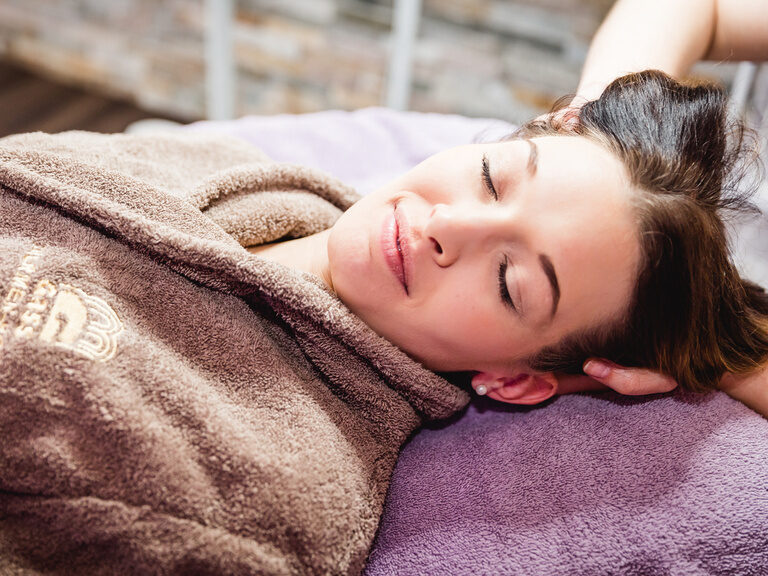 model liegt mit geschlossen augen auf dem rücken und entspannt bei einer sanften massage