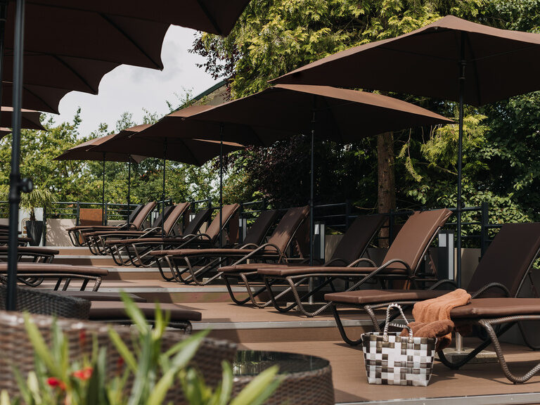 einladende-sonnenterrasse-mit-braunen-moebeln-bequemen-auflagen-erholsamen-relaxliegen-schattenspendenen-sonnenschirmen