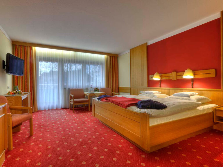 doppelzimmer standard helles möbel rote wand und lampen am bett roter teppich mit blick zum balkon